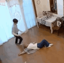 a man is laying on the floor in a living room while another man is standing in front of a table .