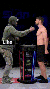 a man in a green hoodie talks to a shirtless man in front of a monster energy drink display