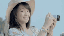 a woman wearing a hat is smiling and holding a camera