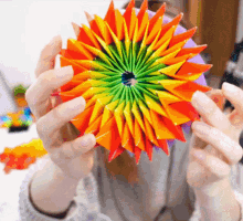 a person is holding a rainbow colored origami flower in front of their face