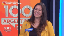 a woman in a yellow jacket is smiling in front of a sign that says 100 argentinas dicen