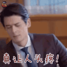 a man in a suit and tie is sitting at a table with his eyes closed and chinese writing behind him .