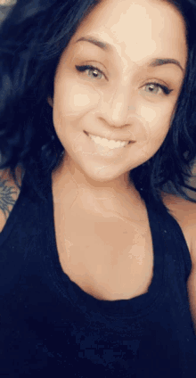 a woman in a black tank top is smiling for the camera