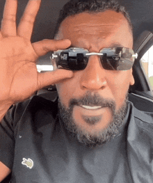 a man with a beard is wearing sunglasses and a black shirt with a lacoste logo