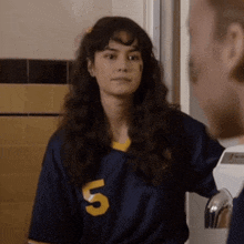 a woman wearing a blue jersey with the number 5 on it is standing next to a man in a bathroom .