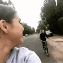 a woman is taking a picture of a man riding a bicycle down a street .