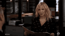 a woman is holding a folder and talking to a man with #svu written on the bottom