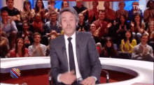 a man in a suit and tie is standing in front of a crowd of people applauding .