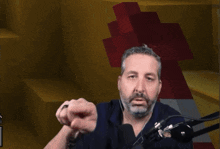 a man with a beard is sitting in front of a microphone with a yellow background