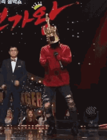 a man wearing a mask and a crown stands on a stage with a microphone