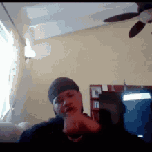 a man wearing a hat is sitting in a living room with a ceiling fan