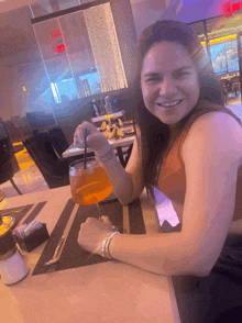 a woman sits at a table with a glass of orange liquid in front of a red exit sign