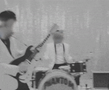 two men in white suits are playing guitars in front of a drum set