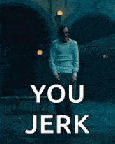a man in a white shirt is standing in a dark room with the words `` you jerk '' written on it .