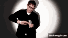 a man wearing glasses and a black jacket is holding a stack of money in his hand .