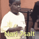 a young boy in a white shirt holds a bottle of nari 7 salt