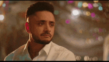 a man with a beard wearing a white shirt is looking at the camera