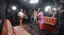 a group of people standing around a red couch with zeus written on the bottom right