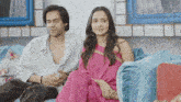 a woman in a pink saree sits next to a man on a couch
