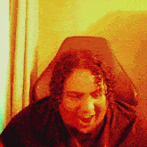 a man with curly hair sits in a chair with his mouth open