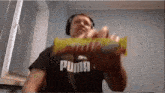 a man wearing a puma shirt is holding a candy bar in his hand