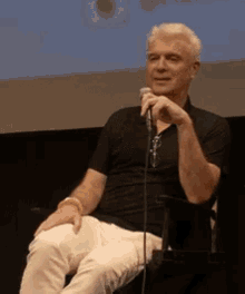 a man in a black shirt is holding a microphone and smiling