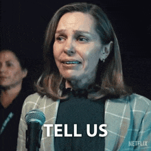 a woman is standing in front of a microphone and saying tell us