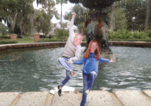 a man and woman jumping in front of a fountain