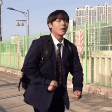 a young man in a suit and tie is running in front of a fence with a sign that says ' a ' on it