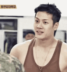 a young man wearing a tank top and a necklace is talking to another man .