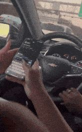 a person is using a phone in a car with a chevrolet logo on the steering wheel