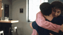 a man in a pink shirt is hugging another man in a black shirt