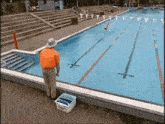 a man in an orange shirt is standing next to a pool