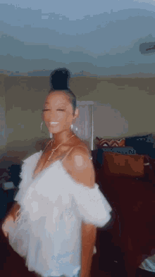 a woman is standing in a living room wearing a white top and earrings .