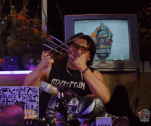 a man wearing a shirt that says led zeppelin holds a pair of claws in front of a television