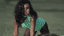 a woman in a green and white polka dot dress is kneeling on the grass .