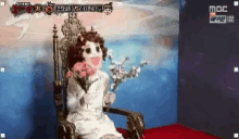 a doll is sitting in a chair with a bouquet of flowers .