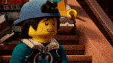a lego character wearing a blue helmet with the letter m on his shirt