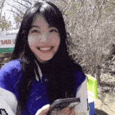 a woman in a blue and white jacket smiles while holding a phone
