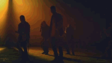 a group of people are dancing in a dark room in front of a yellow light .