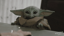 a baby yoda from mandalorian grugu sits on a table with a person