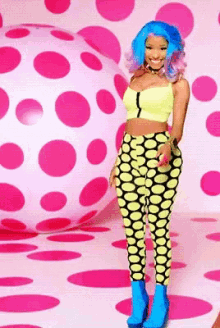 a woman with blue hair and yellow polka dot pants is standing in front of a pink polka dot ball