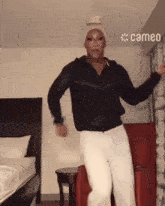 a man in a black shirt and white pants is dancing in a room with a cameo logo on the wall