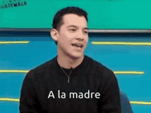 a man wearing a black sweater with the words `` a la madre '' on it is smiling .