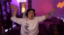 a man wearing headphones and a white shirt is dancing in a room with purple lights .