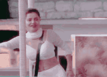 a woman in a white crop top is standing next to a pole .