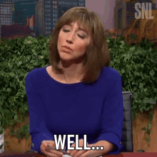 a woman in a blue dress is sitting at a desk and says well