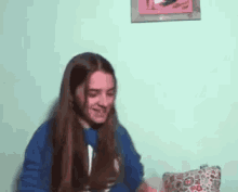a girl with long hair is sitting on a couch in front of a wall with a picture on it .