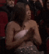 a woman in a pink dress is crying while sitting in a crowd of people .