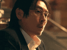 a man wearing glasses and a suit looks to his left